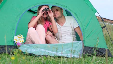 loving couple looking through binoculars sitting in a green tent loving couple looking through binoculars sitting in a green tent rest in the mountains tent camp