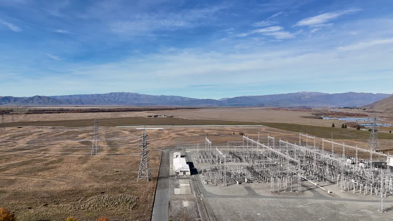 Drone footage captures a vast electrical substation near Lake Tekapo, showcasing its intricate structure against a mountainous backdrop under clear skies