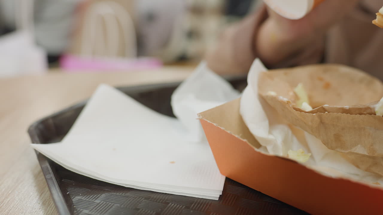 Pulizia disordinata dell'ora di pranzo in sospeso, briciole sparse e macchie di unto rimaste, contenitore di cancelleria con resti di un pasto frettoloso, vassoio di cibo incustodito che mostra segni di una pausa pranzo intensa appena terminata