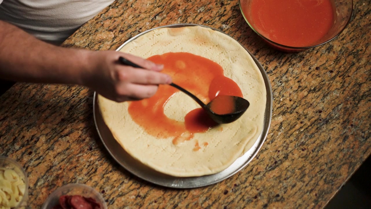 Le mani di uno chef che spalmano una vivace salsa di pomodoro su impasto appena steso