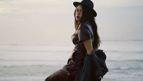 woman posing night beach in elegant hat. girl sitting chair at gloomy seascape.