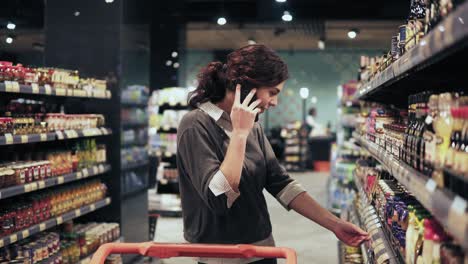 Beautiful-female-buyer-trying-to-choose-products-at-grocery-store-while-speaking-with-someone-on-the-phone