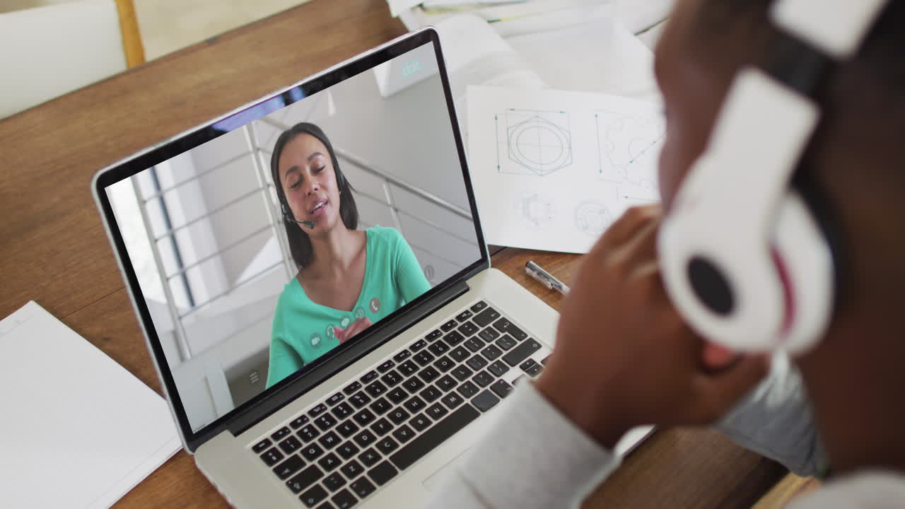 African american male college student wearing headphones having a video call on laptop at home