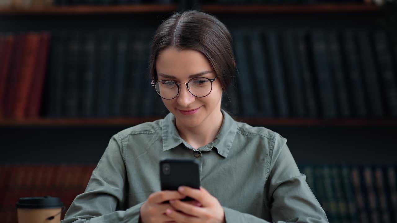 Brunette female student chatting smartphone texting message studying at library enjoy break