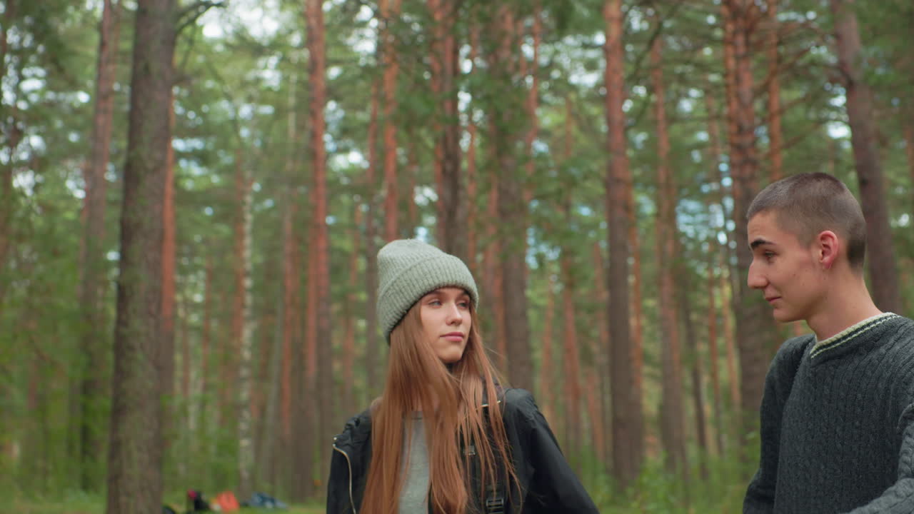 Two young researchers walking through forest stop to take rest, surrounded by tall trees and lush greenery, appearing thoughtful and calm while enjoying tranquil atmosphere of natural environment