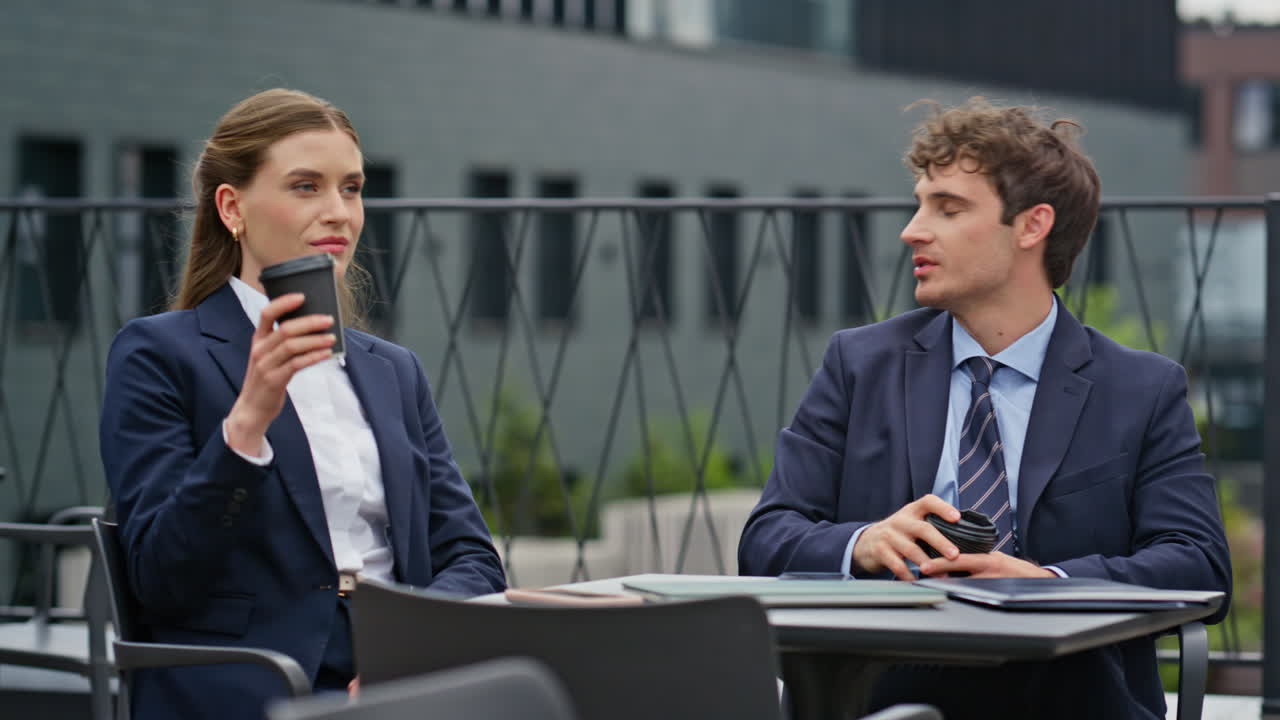 Relaxed business partners drinking coffee together on city office terrace