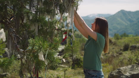 woman ties ribbon and makes wishes on fir tree branch