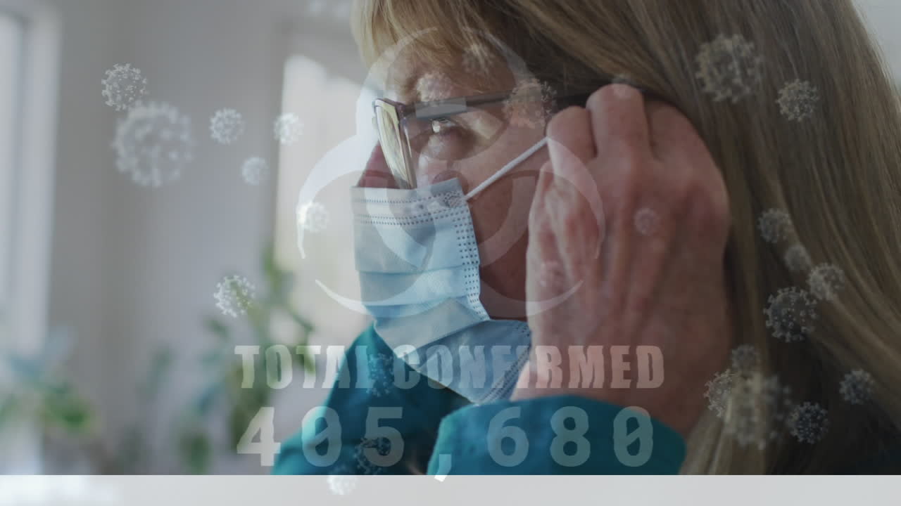 Animation af covid-19 virusceller og et biofare-ikon over en kaukasisk ældre kvinde med ansigtsmaske