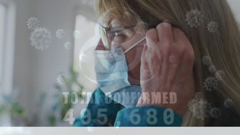 animation of covid 19 virus cells and biohazard icon over caucasian senior woman wearing face mask