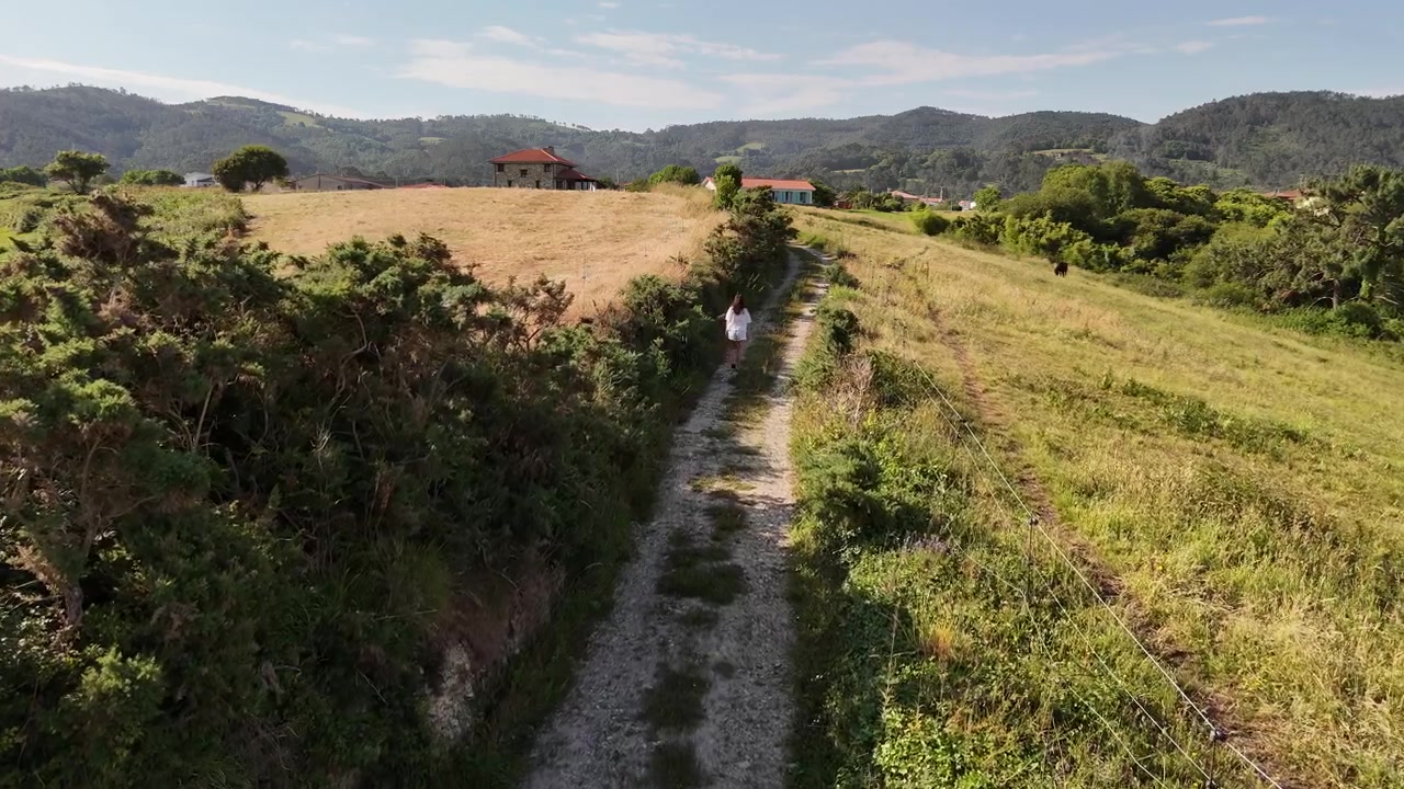 Vista drone di una donna (con liberatoria) che cammina verso le case attraverso campi rurali