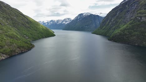 Stunning-aerial-view-of-Sunnylvsfjorden-in-western-Norway---Korsfjorden-and-Geirangerfjord-intersection-to-the-right---Forward-moving-spring-aerial-with-lush-green-forest-and-snow-capped-mountains