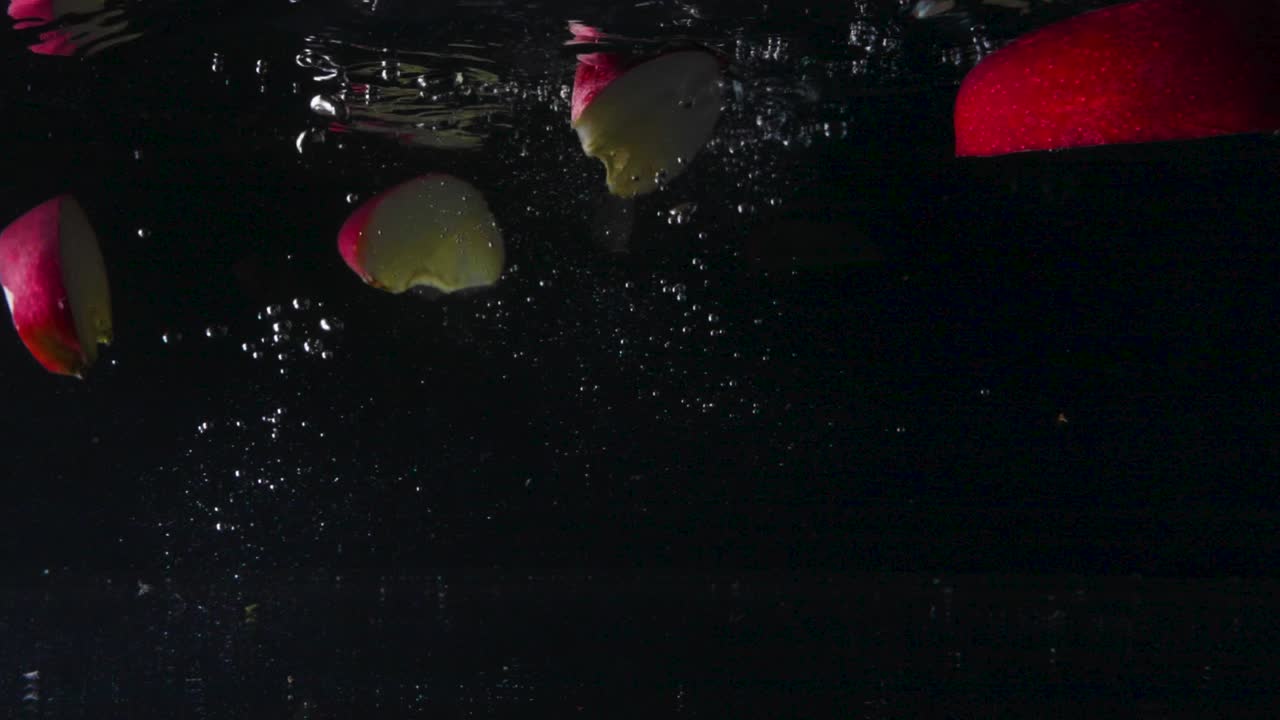 toma submarina en cámara lenta de deliciosas manzanas rojas que caen en el agua y se extienden, luego flotan de nuevo, cierran, cortan