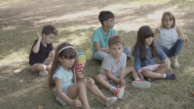 Bambini multietnici seduti sull'erba al parco, che ascoltano qualcuno e parlano.