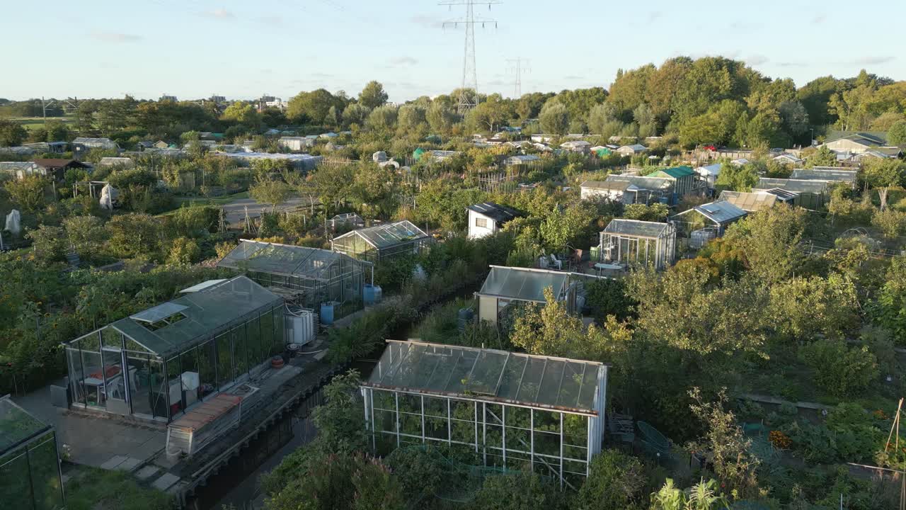 Ripresa con drone di un complesso di orti urbani con piccole serre e appezzamenti, che rappresentano l'agricoltura urbana e la sostenibilità.