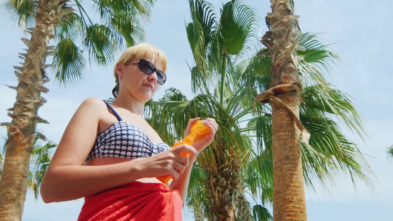 한 여성이 하늘과 야자수 배경에 서 있는 태양의 크림을 사용합니다.