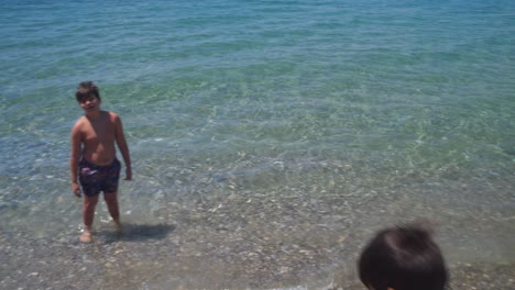 Low-angle-view-of-two-caucasian-brothers,-enjoying-crystal-clear-sea-water-at-beach-of-Kalamata,-Peloponnese,-Greece-4k