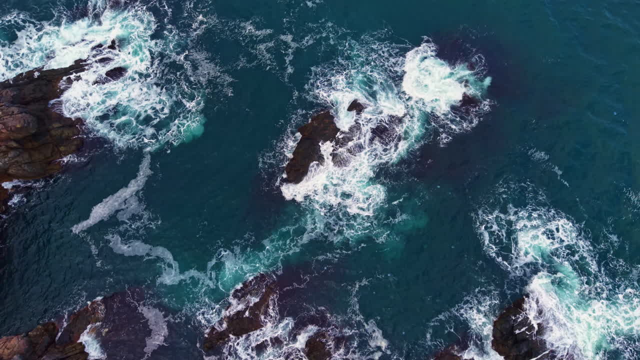 Waves crashing on rugged rocks at a serene coastal location during a sunny afternoon, creating a breathtaking natural display of power and beauty