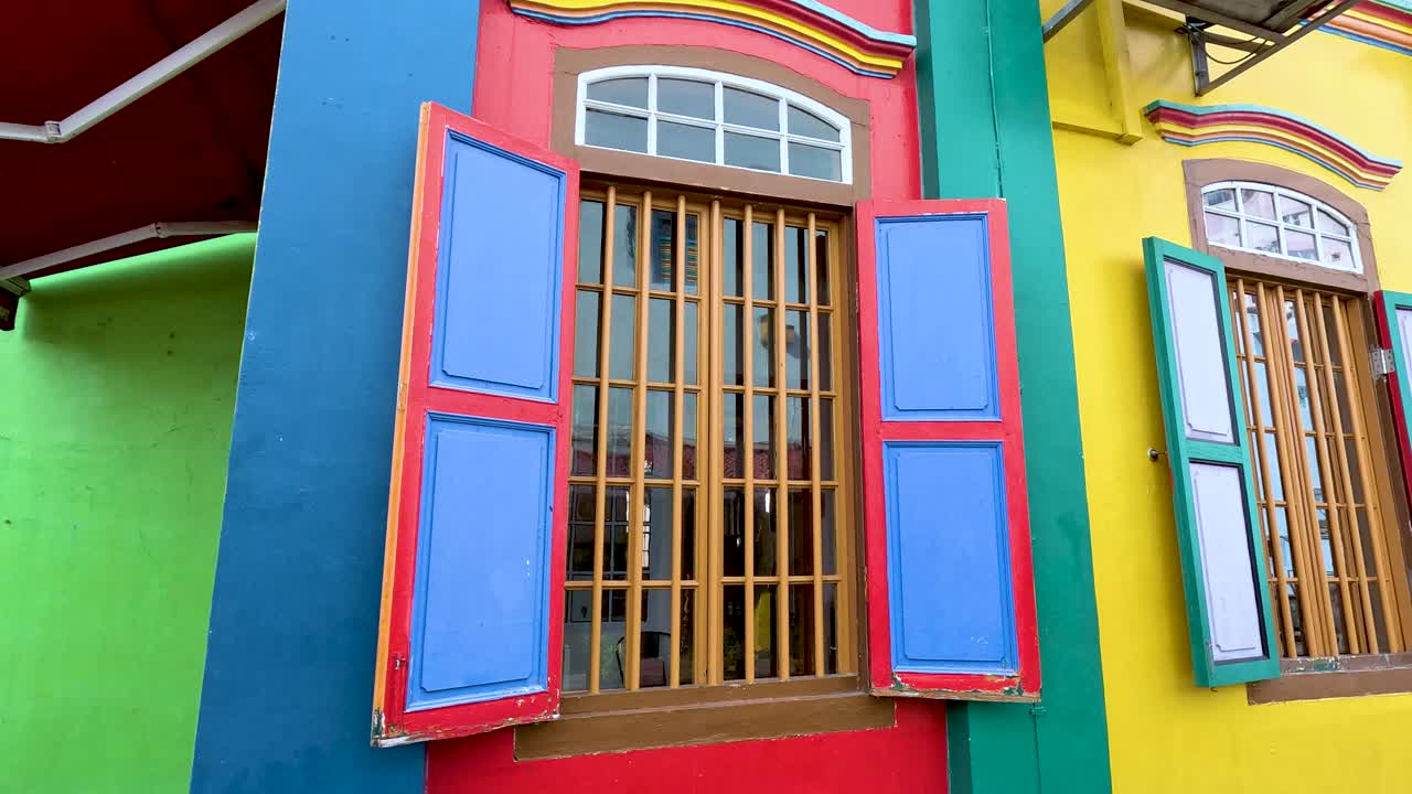 Camera smoothly pans along a vibrantly painted heritage house facade in Singapore, highlighting ornate windows, bold colors, and architectural details in daylight