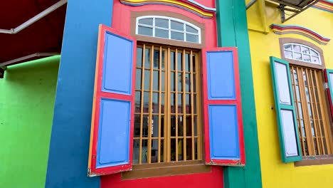camera smoothly pans along a vibrantly painted heritage house facade in singapore, highlighting ornate windows, bold colors, and architectural details in daylight