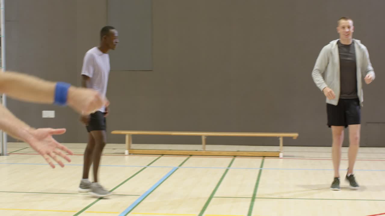 Coach in grey hoodie clapping and demonstrating, 4 men practicing sets with volleyballs to improve