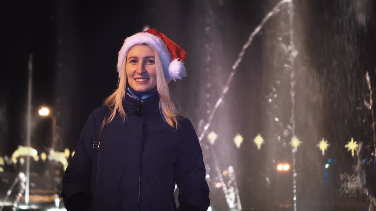 girl looks at camera against the background of a fountain in a Santa Claus hat