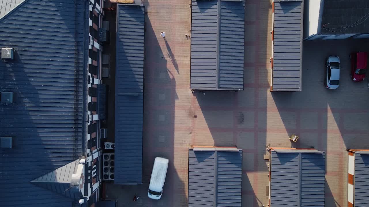 vista aérea de arriba hacia abajo de pequeñas viviendas en el mercado de liepaja después del amanecer, a principios de la mañana de verano, calles vacías, techos de metal gris, autos casuales, tiro de drones de ojo de pájaro de gran angular moviéndose a la derecha