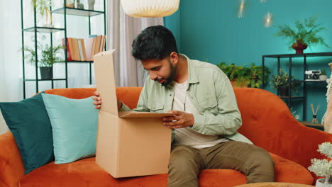 Happy-Arabian-man-shopper-unpacking-cardboard-box-delivery-parcel-online-shopping-purchase-at-home