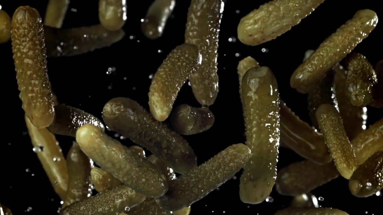 Chute de cornichons et de gouttes d'eau au ralenti sur fond noir