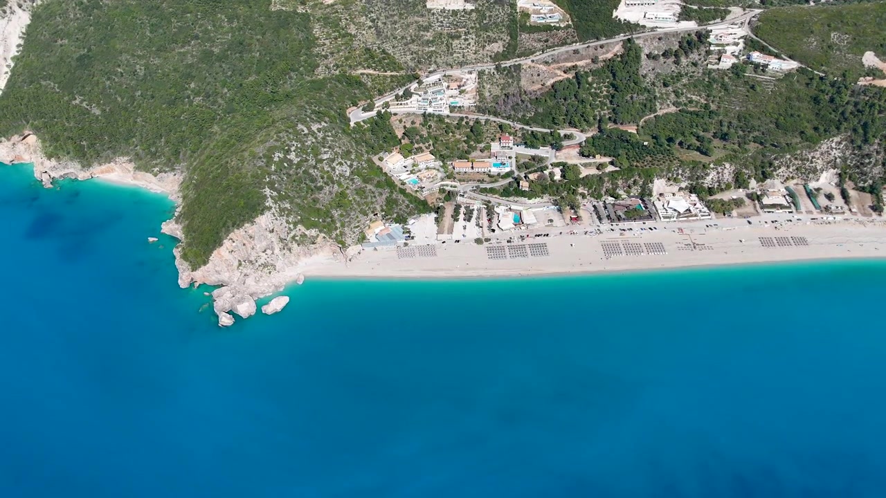 Turkuaz bir plajın, kıyı tesisinin ve kristal berraklığında denizin kuşbakışı drone görüntüsü. Kayalıklar ve Akdeniz manzarasıyla doğal sahil şeridi.