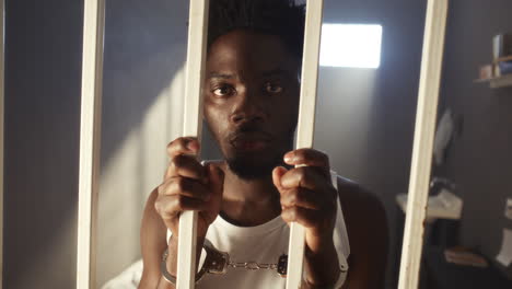 portrait of handcuffed black inmate standing behind prison bars
