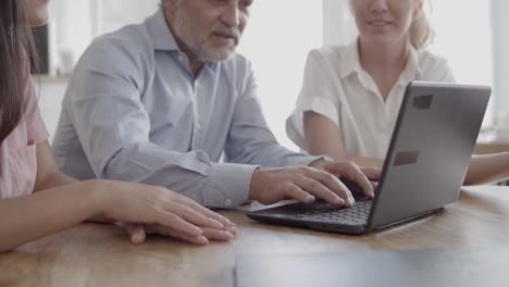 vista recortada del hombre de negocios senior escribiendo en el teclado de la computadora portátil con compañeros de equipo a su lado