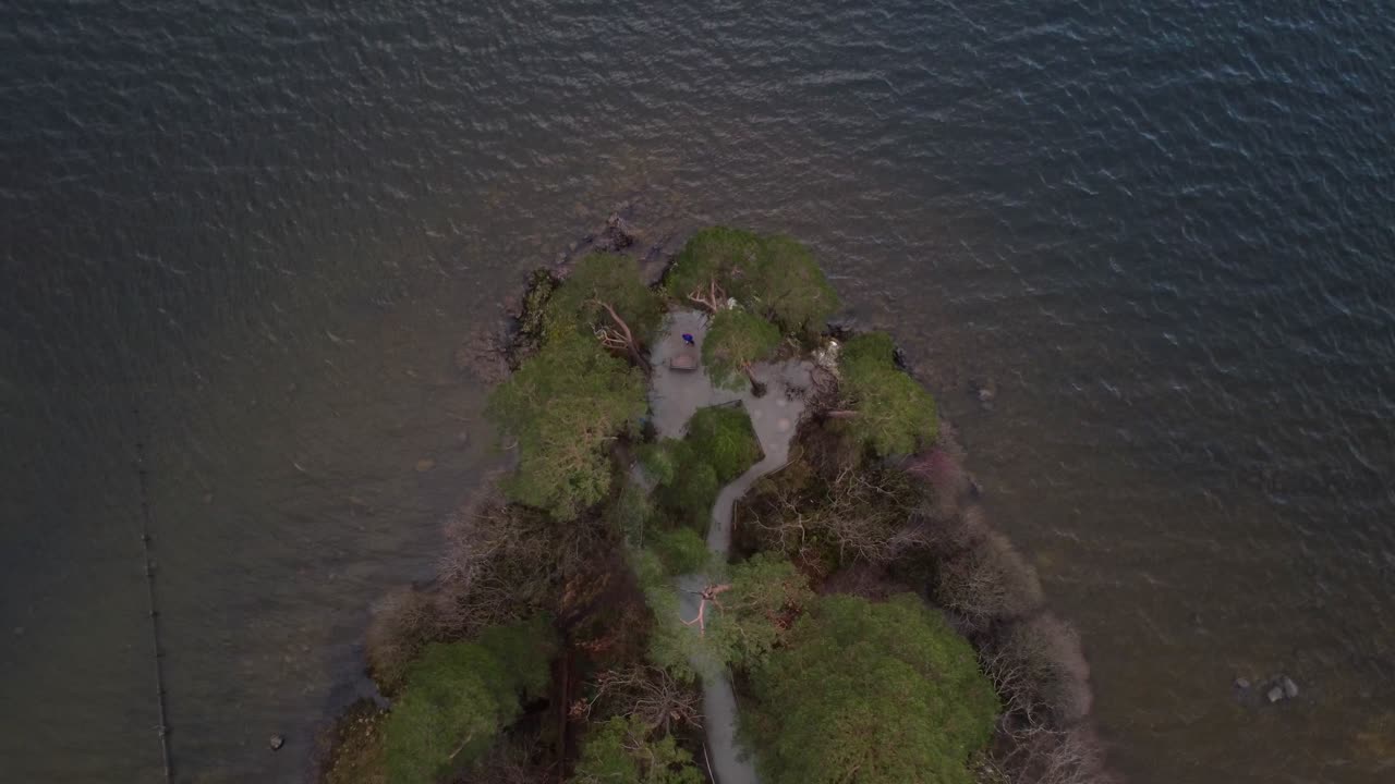 Aerial drone shot looking down onto ripples in water of lake and peninsula, at Friar's Crag in Keswick