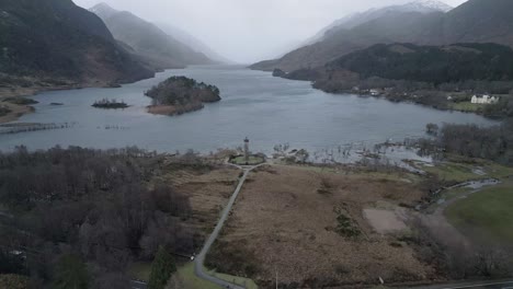 Glenfinnan-viaduct-in-scotland-with-lush-landscape,-serene-loch,-and-moody-skies,-aerial-view