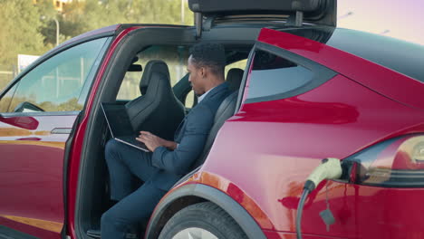 un hombre de negocios trabajando en una computadora portátil dentro de un coche eléctrico rojo