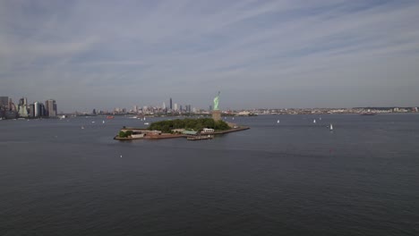 aerial view towards the liberty island, surrounded by ferries and sailboats, in sunny new york, usa - rising, drone shot