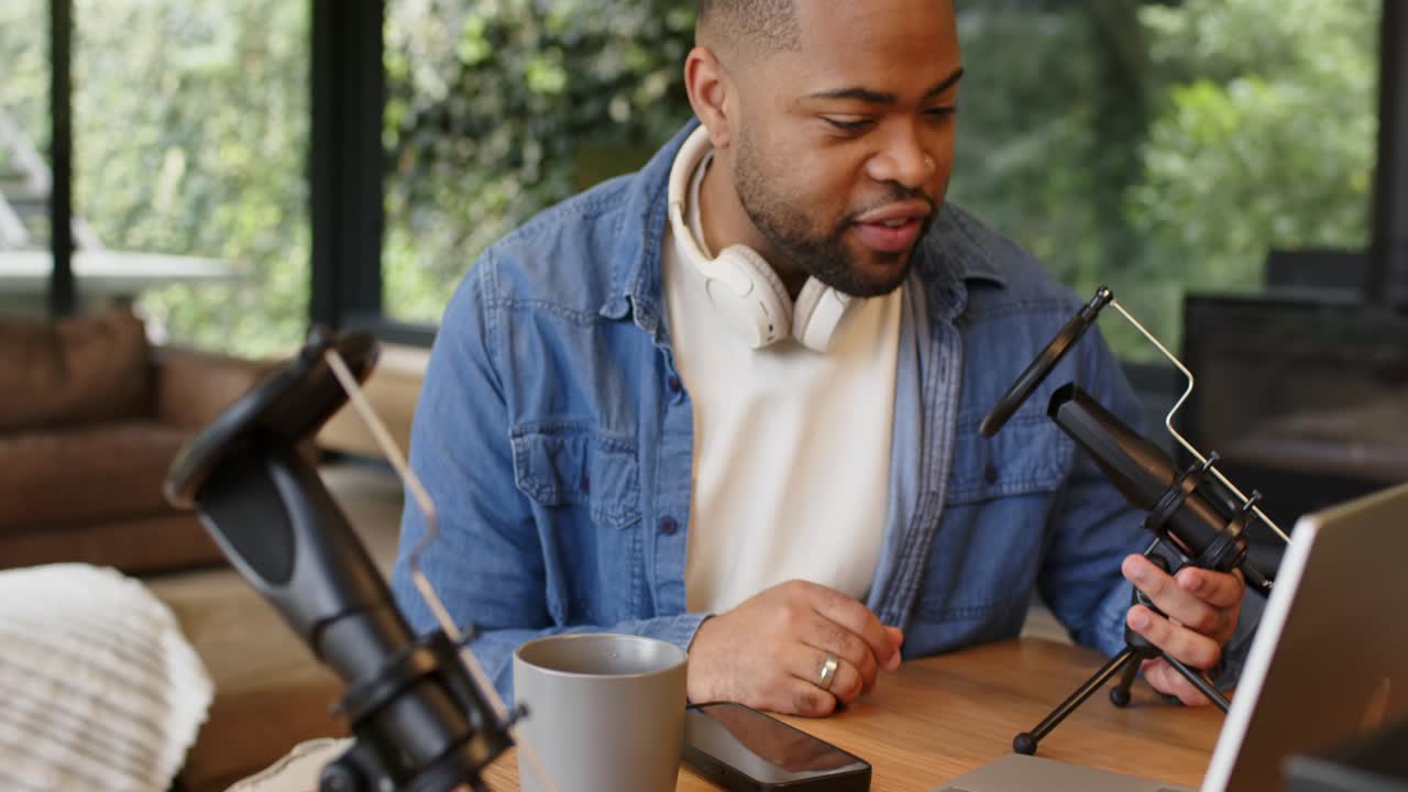 African American man typing on laptop and adjusting mic, headphones in home studio preparing stream