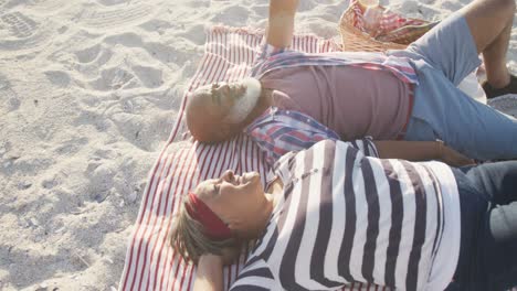 happy senior african american couple lying on blanket at beach, slow motion