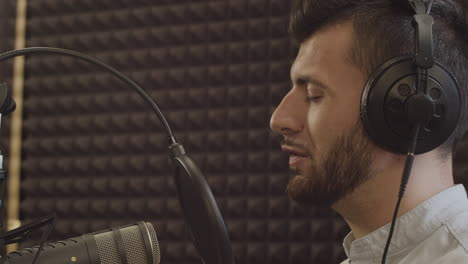 primer plano de un joven presentador de radio con barba y aparatos ortopédicos despidiéndose de sus oyentes y quitándose los auriculares