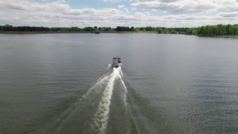 drone aéreo disparado sobre un bote de motor blanco acelerando sobre el agua del lago en un día nublado