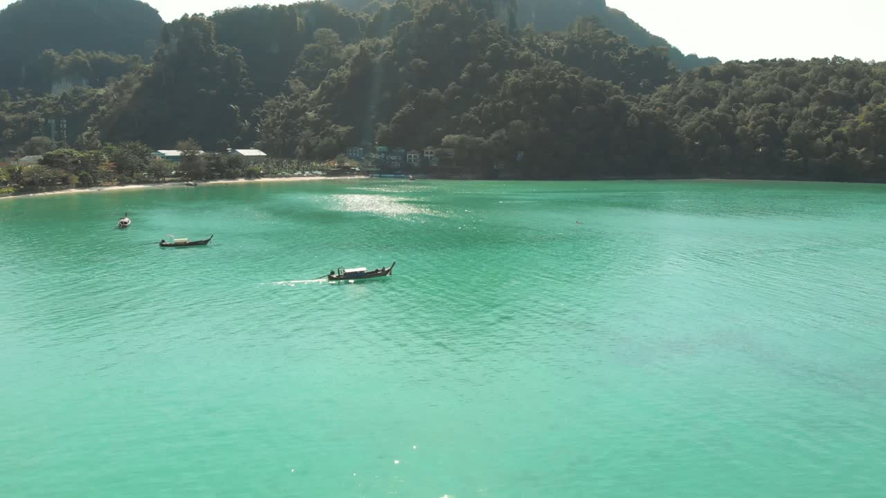 Long-tail boat setting sail from Ko Phi Phi Island tearing through Emerald Green sea in Thailand - Aerial tracking shot