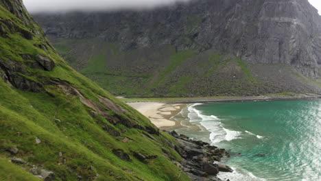 desciende y revela una toma de avión no tripulado de la aislada playa de kvalvika en las islas lofoten de noruega, una toma aérea cinematográfica con agua azul turquesa