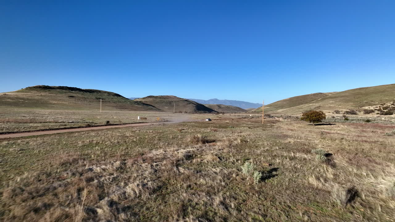 tomada aérea de un coche conduciendo por un camino de tierra en willcox, arizona, siguiendo una toma de avión no tripulado con montañas en el fondo