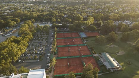 aerial cinematic shot of a private sport club with tennis courts, a golf field and a parking lot at golden hour