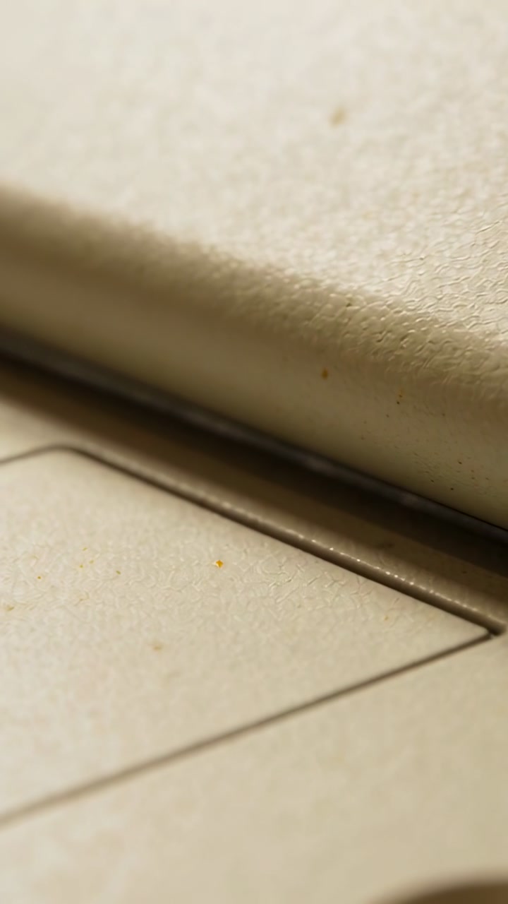 Vertical video: Panning camera revealing beige hinge on desk for inspection, exposing seam and dust