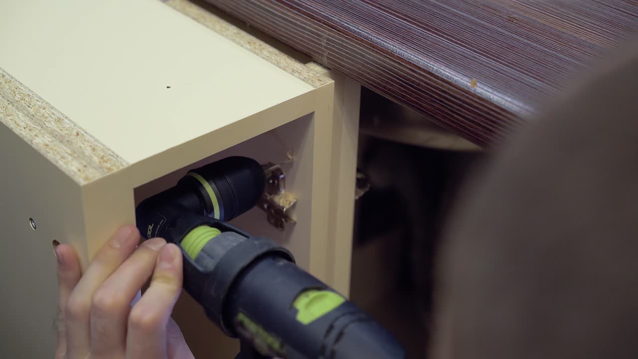 Furniture maker drills the side surface of the cabinet using a corner nozzle on the drill Close-up