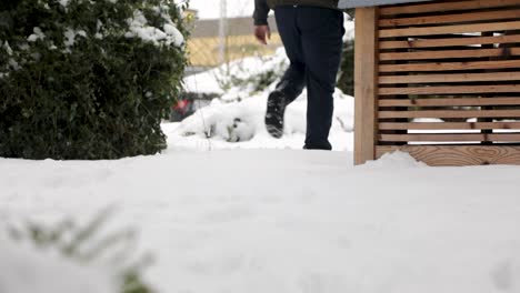 low angle slowmotion of person walking through deep snowy garden after strong snowfall in winter