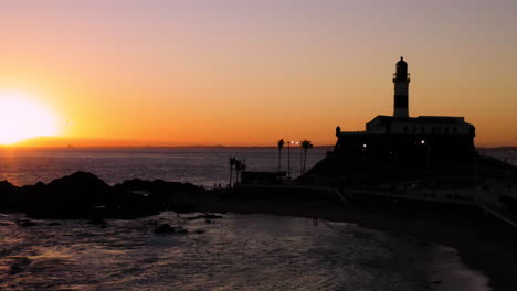 Aerial-view-of-Farol-da-Barra-illuminated-by-the-sun-and-the-sea,-at-sunset,-Salvador,-Bahia,-Brazil