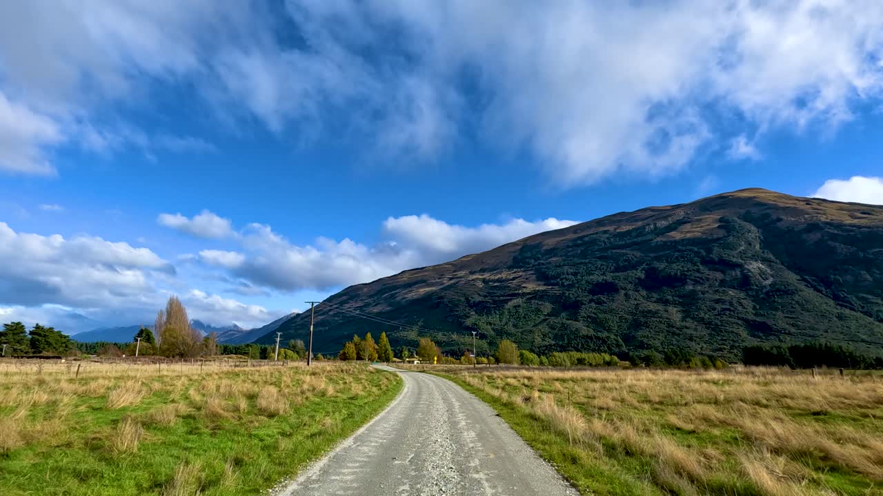 Vehicle travels along rural gravel road with mountain views, daylight, wide angle, steady forward motion