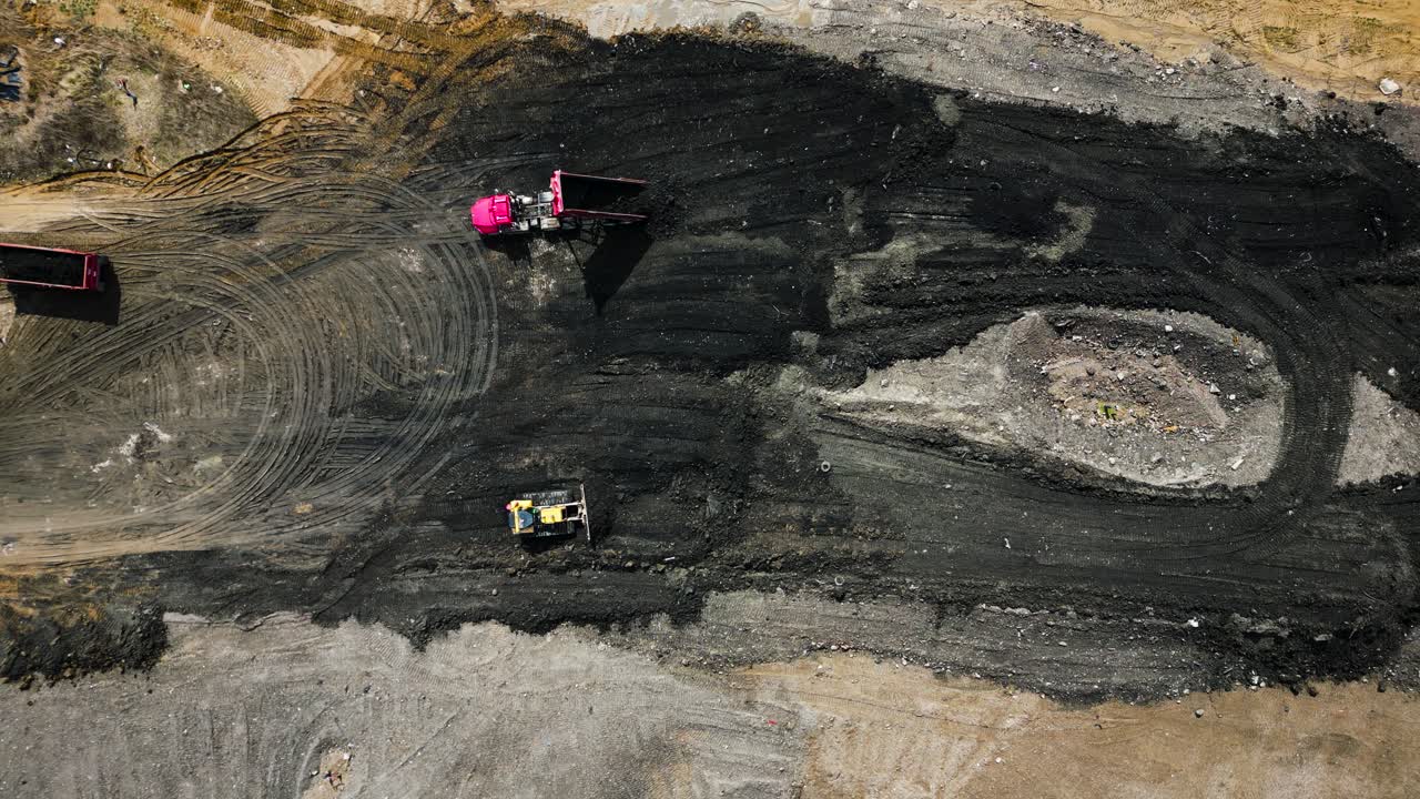 Overhead drone shot looking down on a construction site where bulldozers and dump trucks are moving dirt on a bright, sunny day