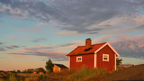 Casa-Tradicional-De-Madera-Roja-En-La-Isla-Con-Puente-Al-Atardecer-Cielo-De-Nubes-En-Suecia